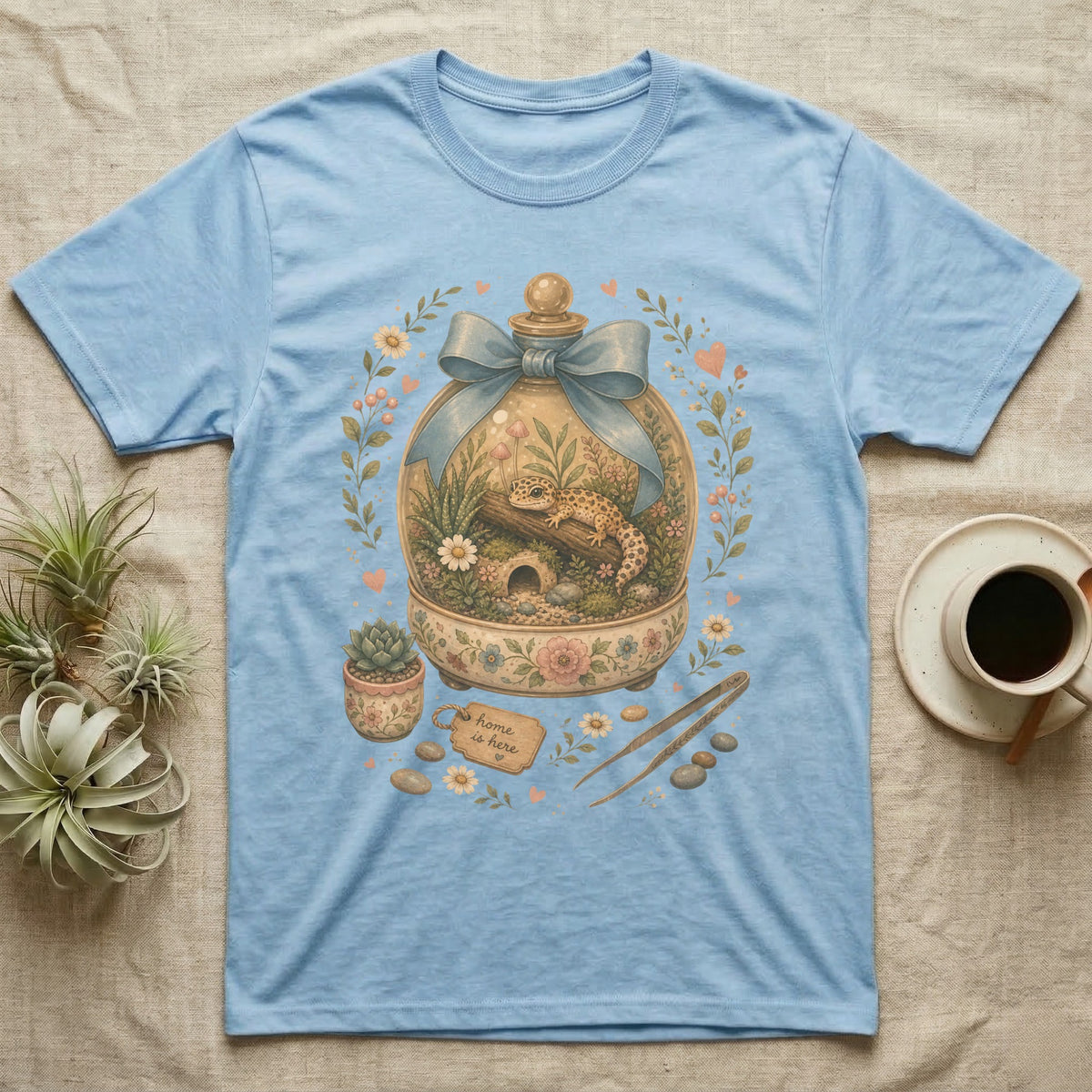 Light blue t-shirt with a terrarium design featuring a gecko and floral accents.