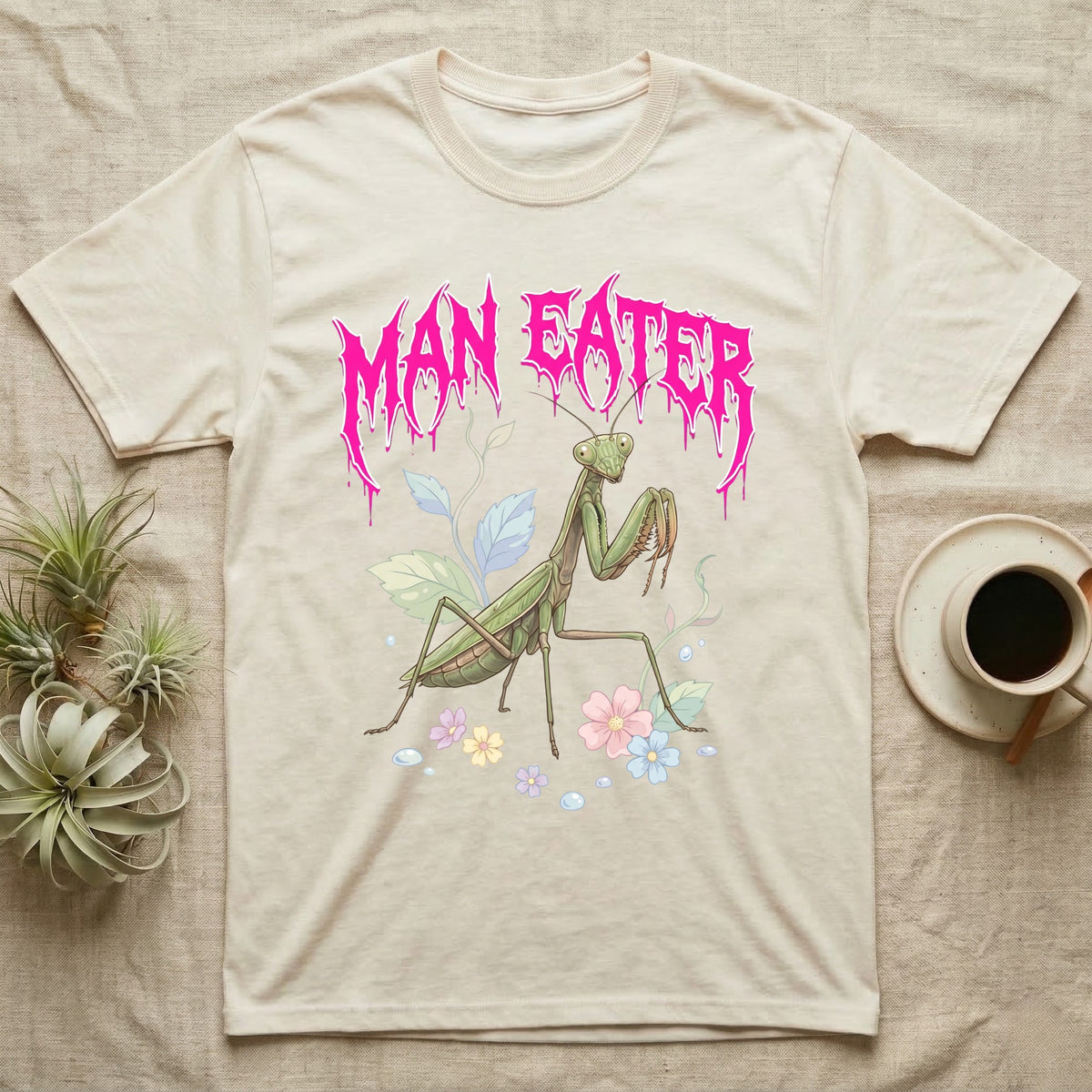 Chinese Mantis Feral T-Shirt in Natural — Pastel Chinese mantis with raised spiked forelegs among leaves and blossoms, jagged magenta metal wordmark "MAN EATER" above.