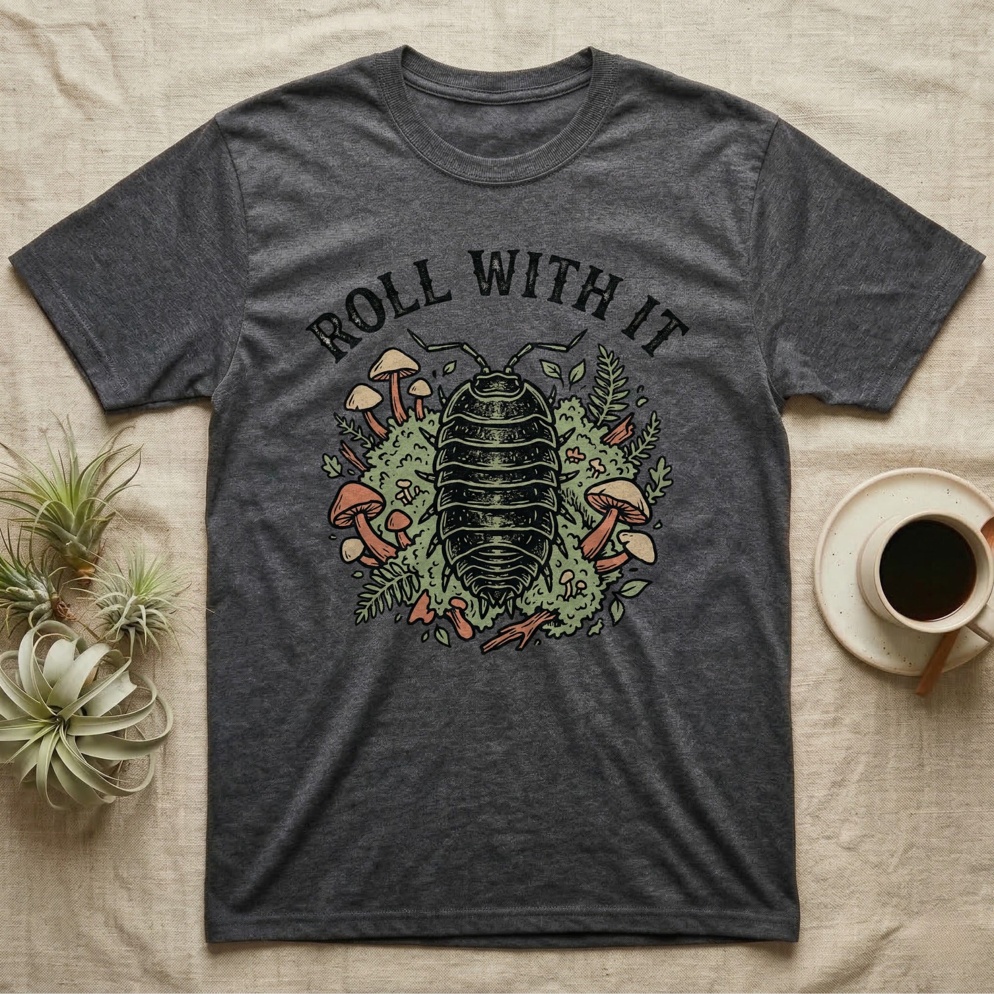 Dark grey t-shirt with an illustration of a pill bug surrounded by mushrooms and foliage.