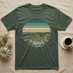 Ball Python Monstera T-Shirt in Military Green — Ball python coiled through a striped rainforest circle window with monstera and pothos on a near-black tee