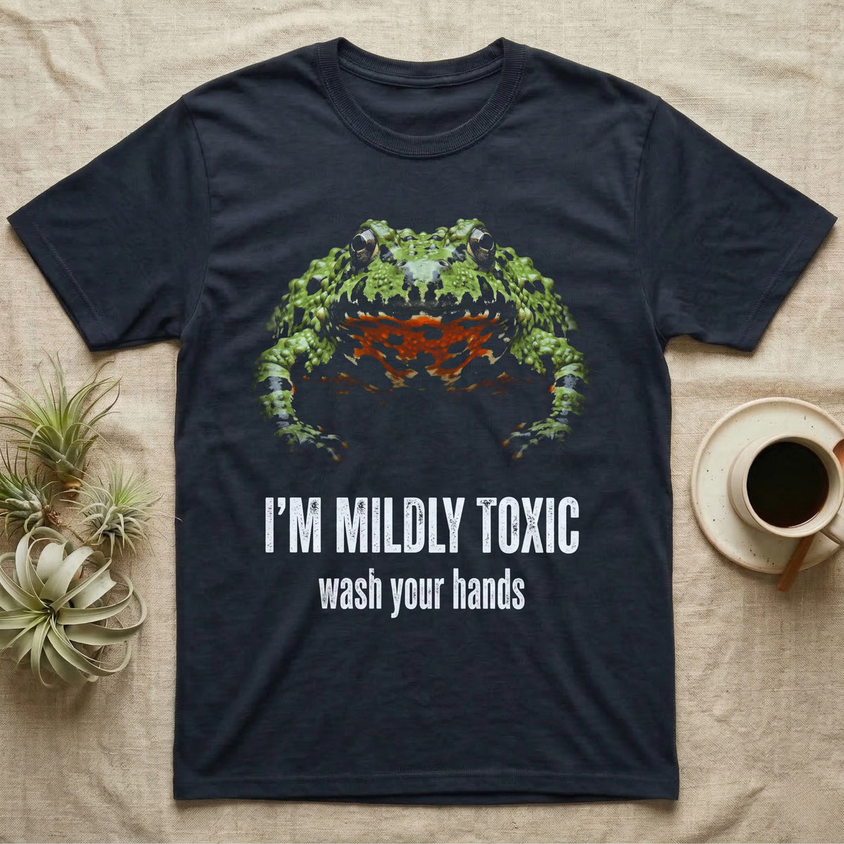 Deadpan mugshot of an olive-green fire-bellied toad on black, captioned I'm mildly toxic, wash your hands. — shown on a Navy tee.
