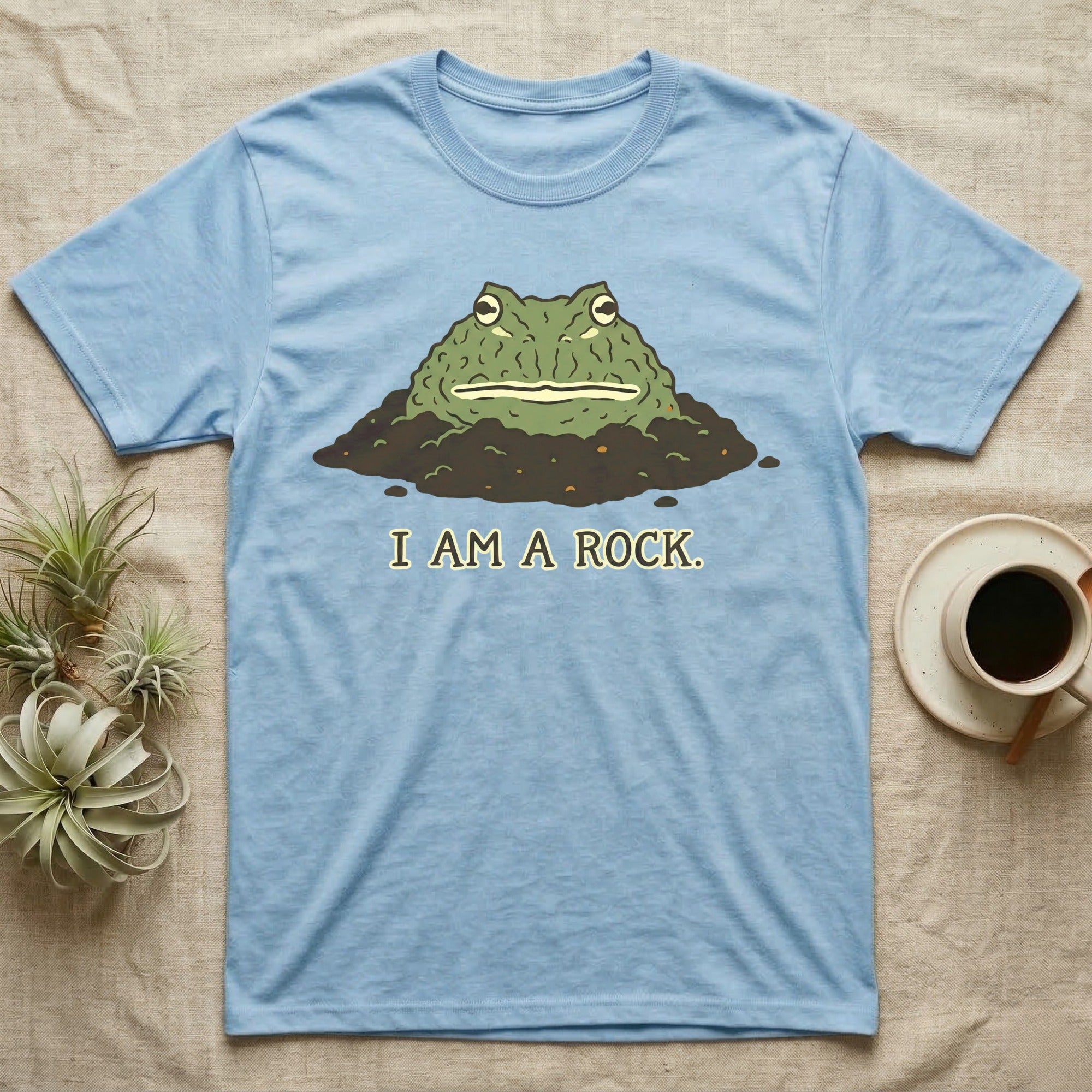 Light blue t-shirt with a cartoon frog peeking out of dirt, text "I AM A ROCK."
