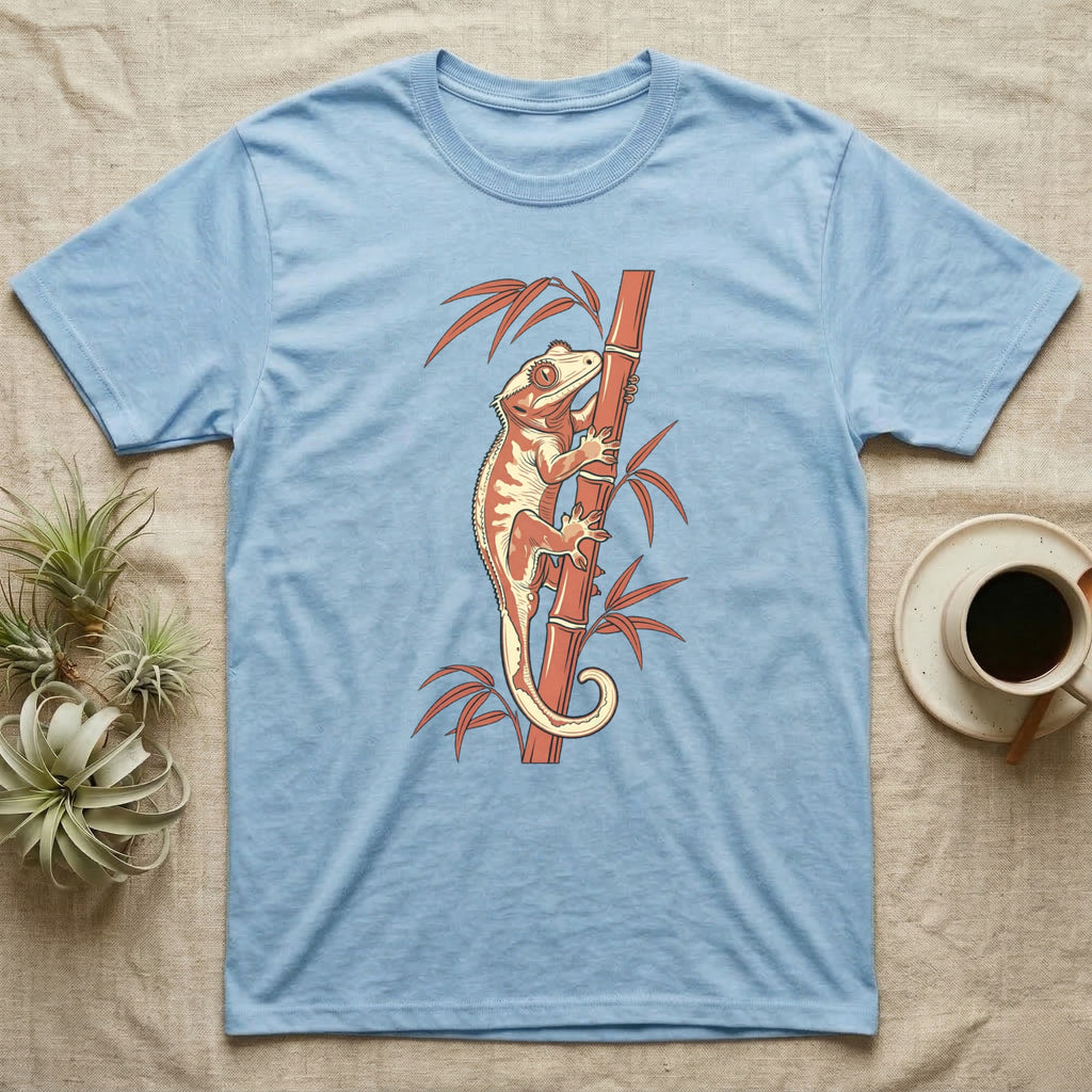 Crested gecko climbing a bamboo stalk on a light blue t-shirt.