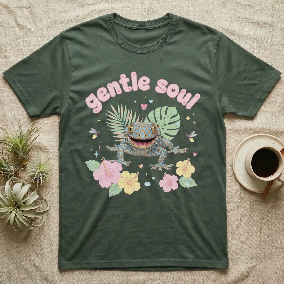 Tokay Gecko Baby T-Shirt in Military Green — Blue-and-orange spotted tokay gecko among pastel leaves and hibiscus under puffy pink bubble text "gentle soul".
