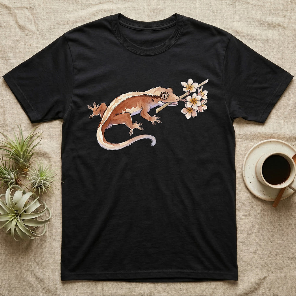 Crested Gecko Blossom T-Shirt in Black — Watercolor illustration of a rust-brown crested gecko holding a frangipani blossom sprig, on a dark grey t-shirt.