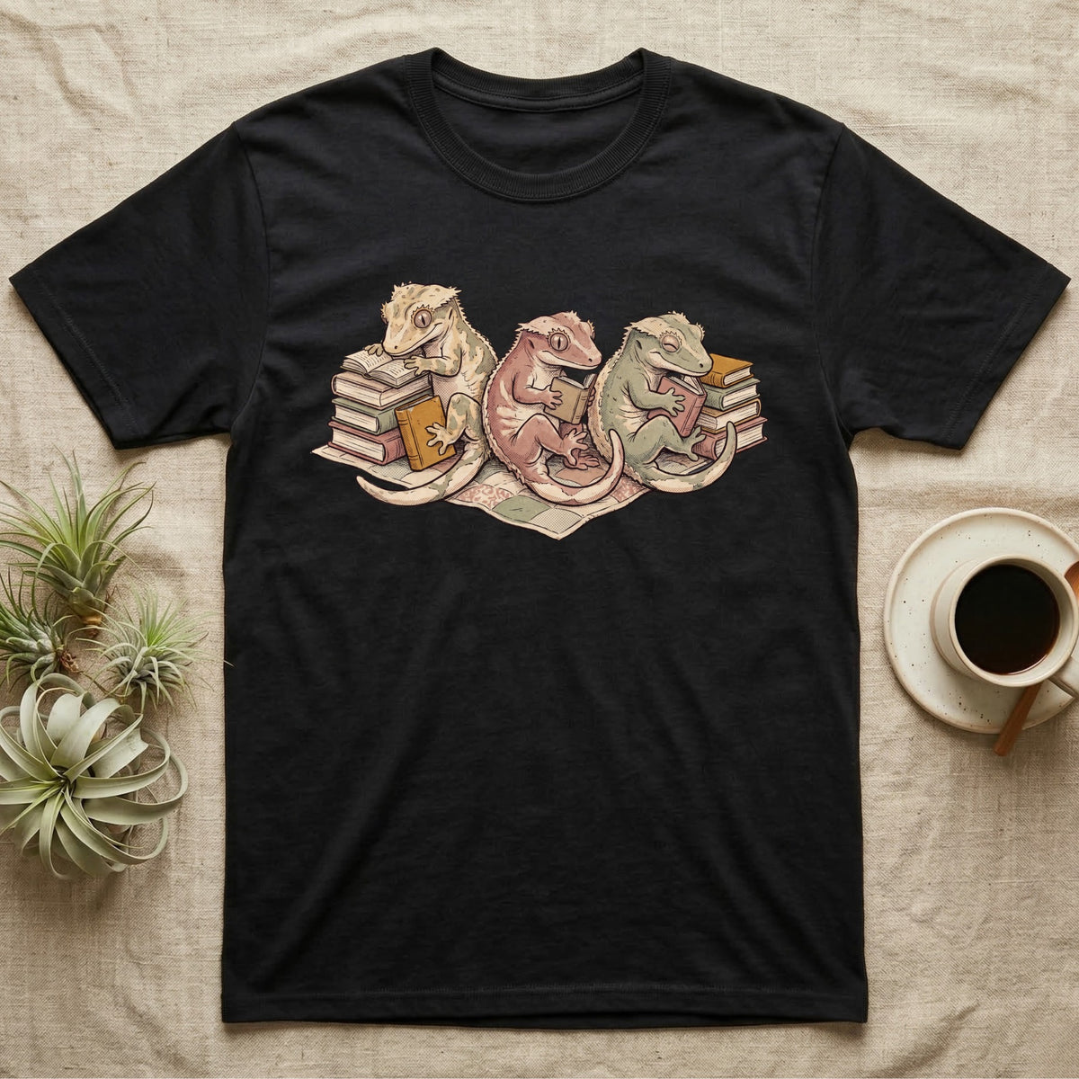 Gecko Book Club T-Shirt in Black — Warm storybook illustration of three crested geckos in a cozy reading row, each beside a tiny stack of books.