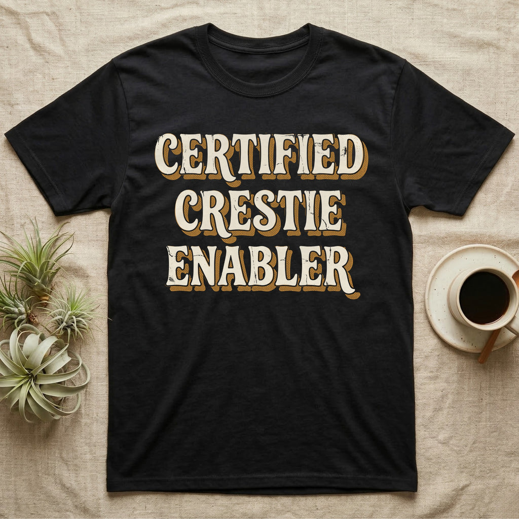 Certified Crestie Enabler T-Shirt in Black — Bold retro drop-shadow wordmark reading "Certified Crestie Enabler" in cream and ochre on a grey background.