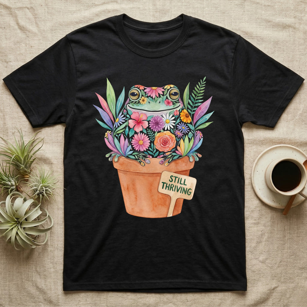 Tree Frog Thriving T-Shirt in Black — A White's tree frog made of watercolour flowers, sitting in a terracotta pot with a plant label reading STILL THRIVING.