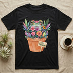 Tree Frog Thriving T-Shirt in Black — A White's tree frog made of watercolour flowers, sitting in a terracotta pot with a plant label reading STILL THRIVING.
