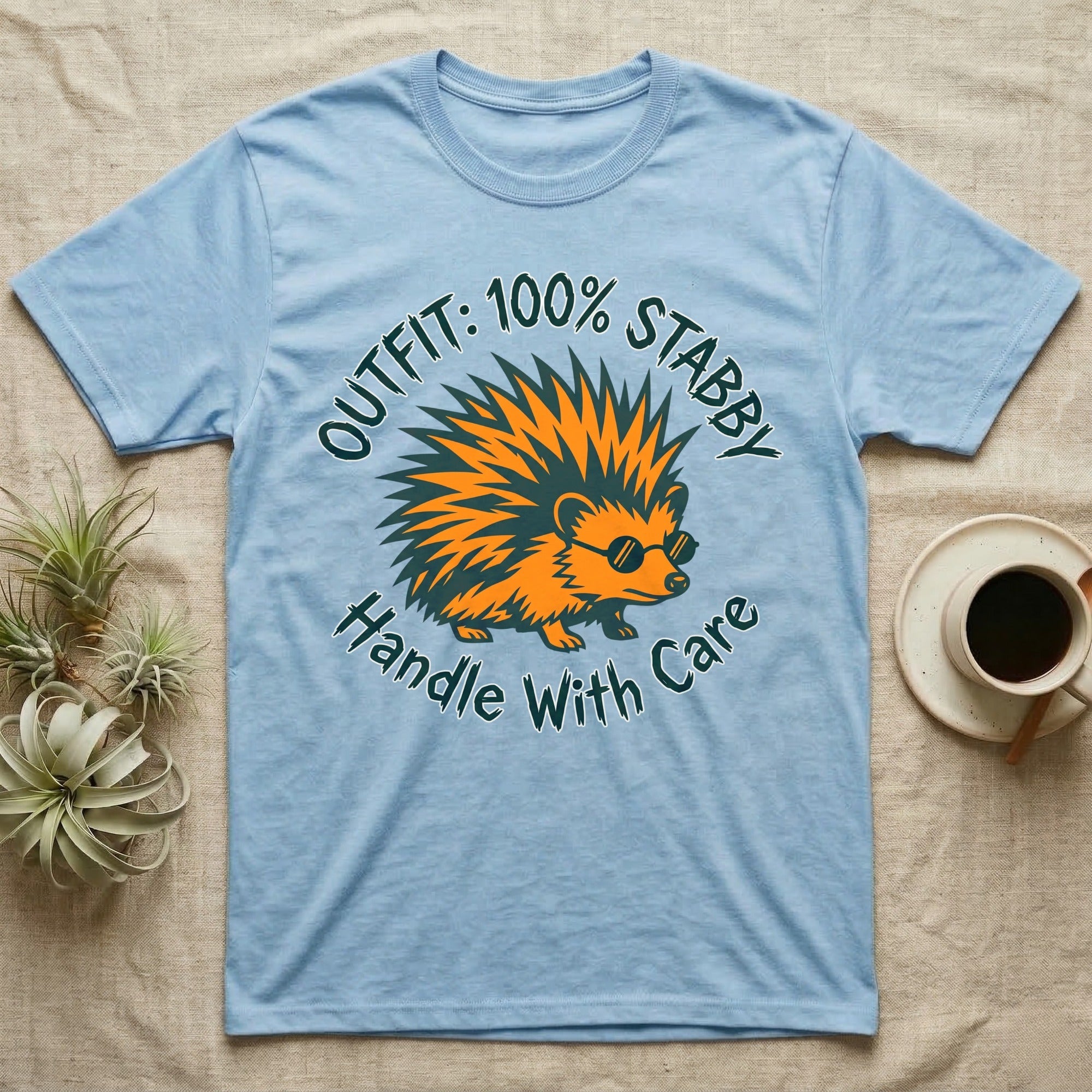 Light blue t-shirt with a cartoon hedgehog wearing sunglasses and the text "Outfit: 100% Stabby. Handle With Care."