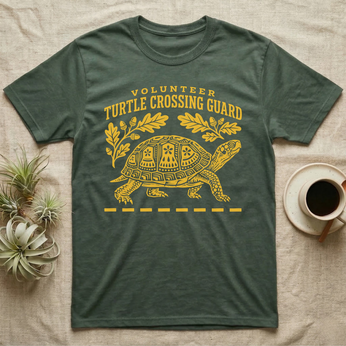 Box Turtle Crossing T-Shirt in Military Green — Yellow folk-print eastern box turtle walking across a dashed road line with oak leaves, text Volunteer Turtle Crossing Guard