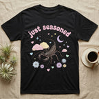 Giant Vinegaroon Baby T-Shirt in Black — Pastel giant vinegaroon with pincers and whip tail among rocks and a crescent moon, puffy pink wordmark "just seasoned" above.