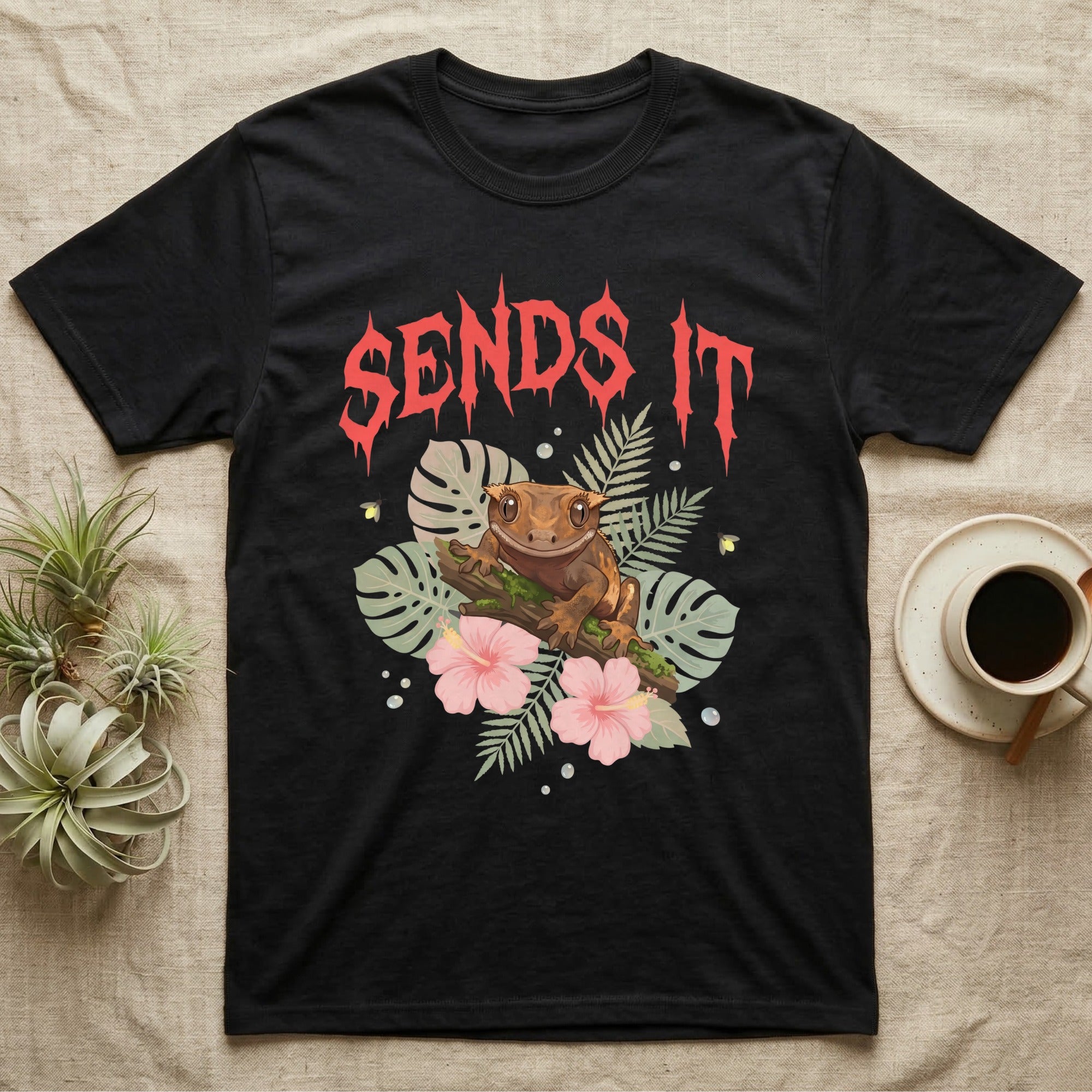Crested Gecko Feral T-Shirt in Black — Crested gecko on a mossy branch in a pastel jungle scene under a spiky coral metal wordmark reading SENDS IT.