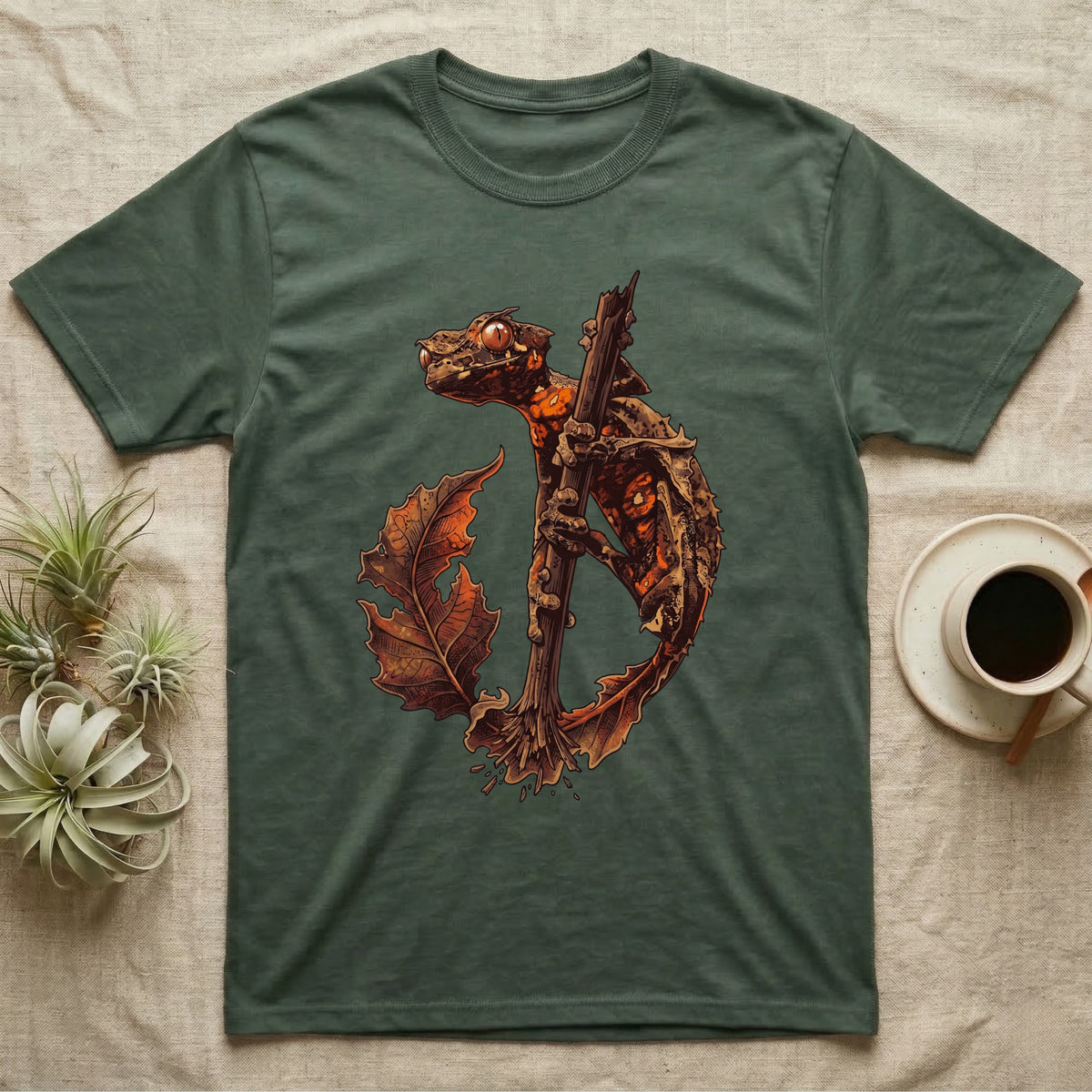 Vintage ink illustration of an eyelash leaf-tailed gecko clinging to a branch with its tail curled beside a serrated leaf, no on-shirt text. — shown on a Military Green tee.