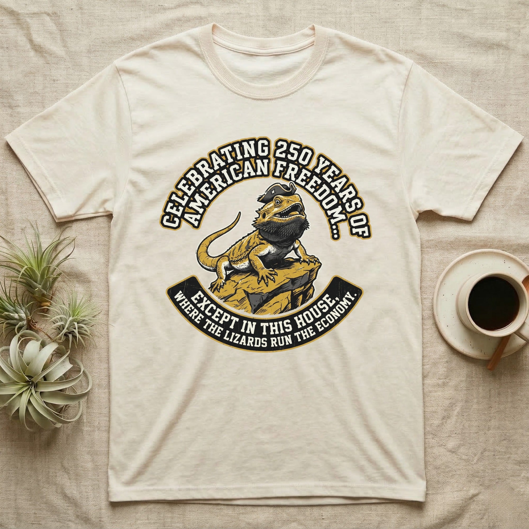 Bearded Dragon 1776 T-Shirt in Natural — Bold woodcut tee of a bearded dragon in a tricorn hat black-bearding on a rock, gold and cream banner reading the lizards run the economy.