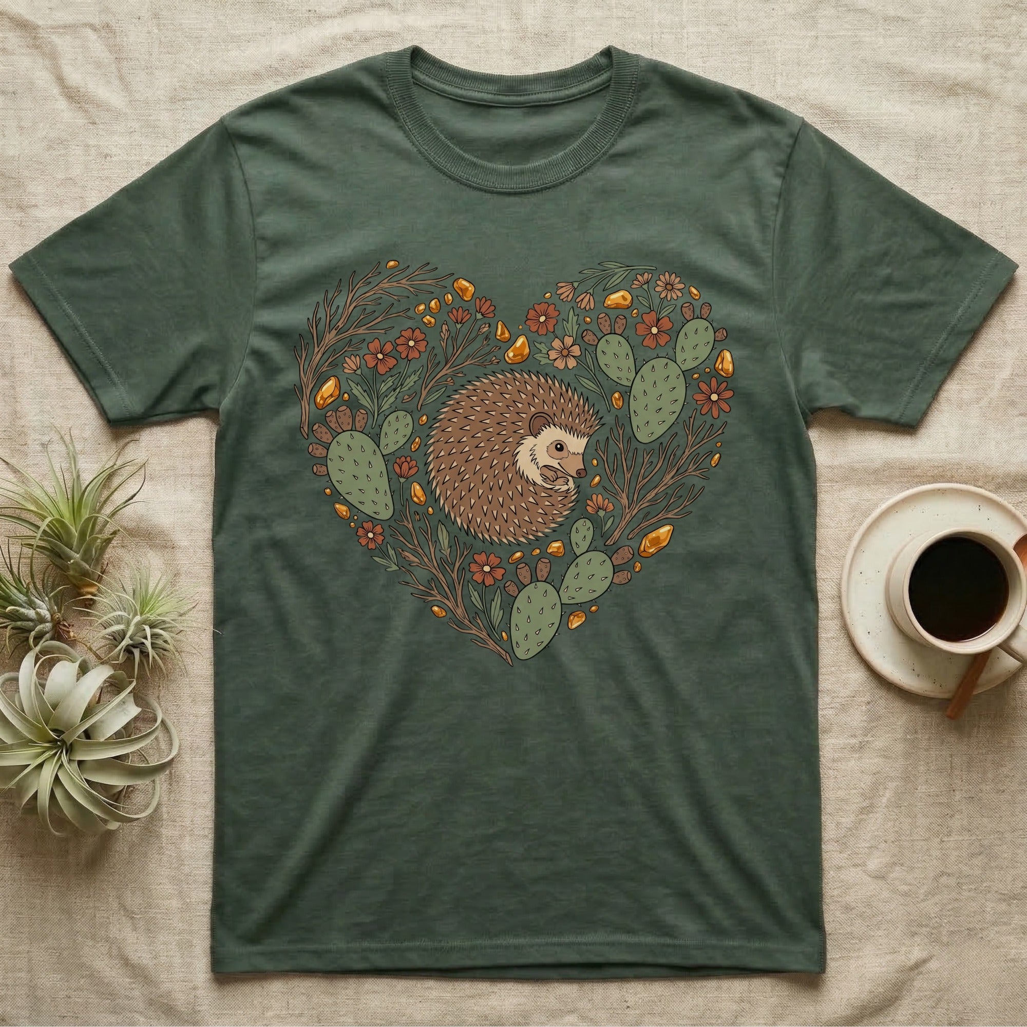 Green t-shirt with a heart-shaped design of a hedgehog, cacti, and flowers.