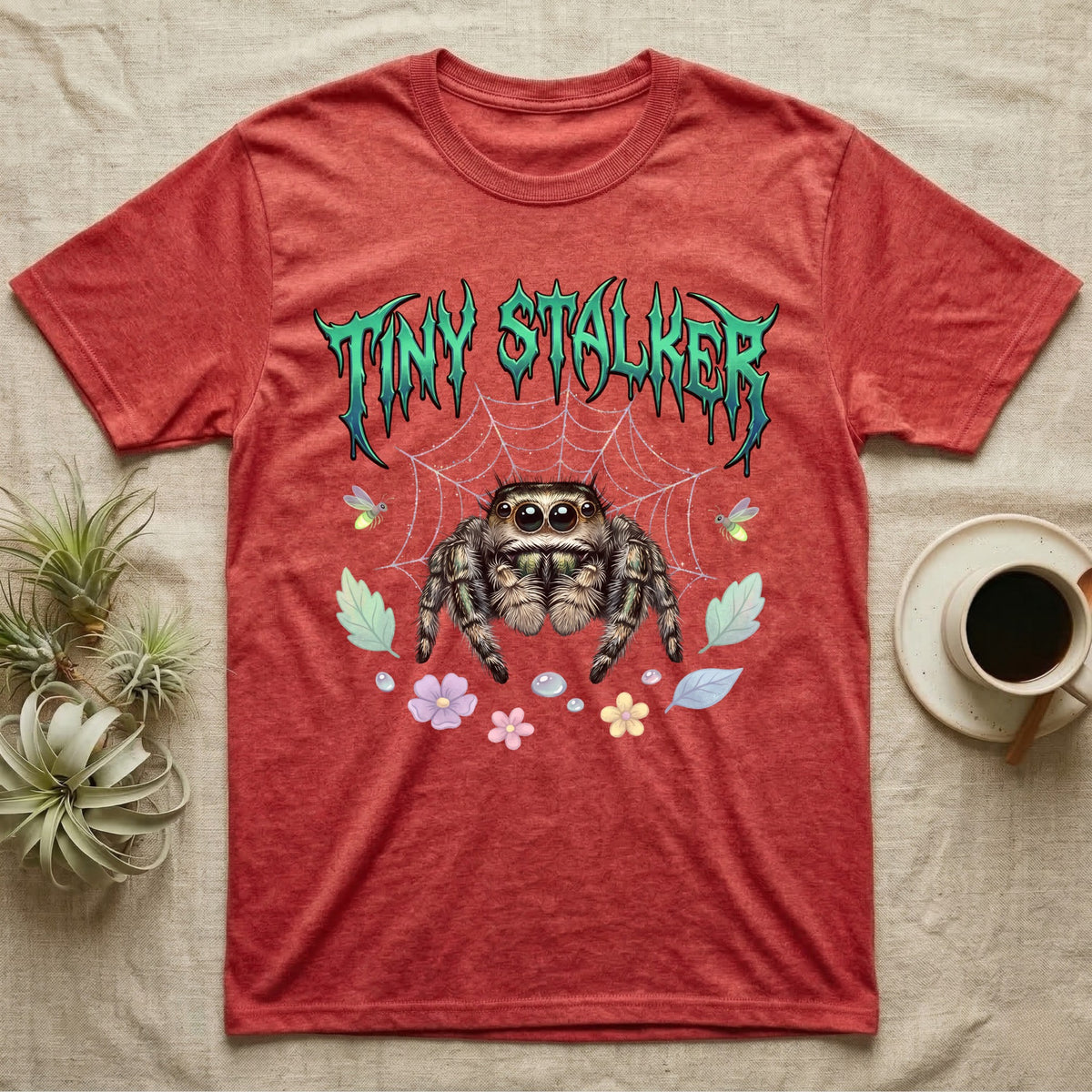 Regal Jumping Spider Feral T-Shirt in Heather Red — Fuzzy jumping spider with huge eyes in a pastel garden under a spiky iridescent-teal metal wordmark reading TINY STALKER.