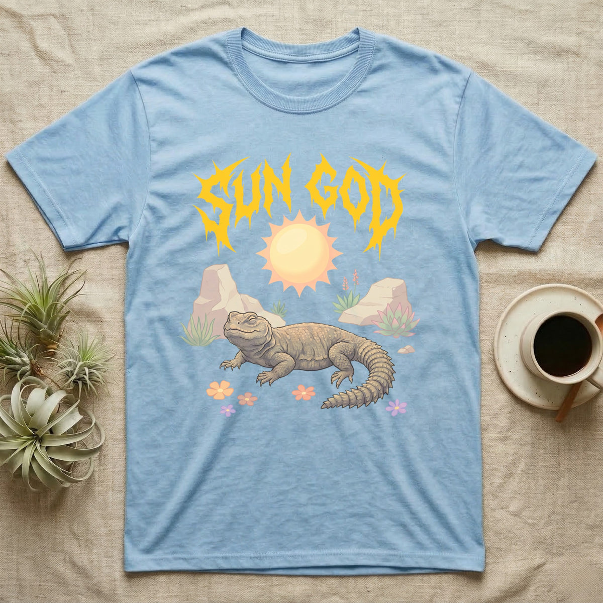 Moroccan Uromastyx Feral T-Shirt in Light Blue — Moroccan uromastyx basking under a big sun with a jagged solar-gold metal "SUN GOD" wordmark and pastel desert scene.