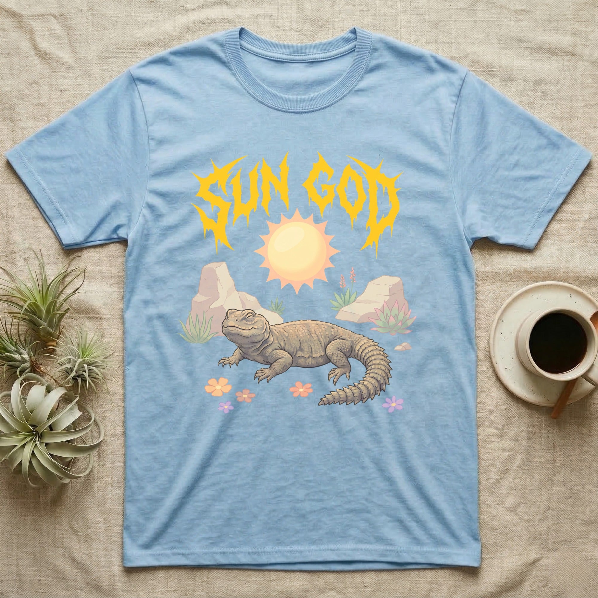 Moroccan Uromastyx Feral T-Shirt in Light Blue — Moroccan uromastyx basking under a big sun with a jagged solar-gold metal "SUN GOD" wordmark and pastel desert scene.
