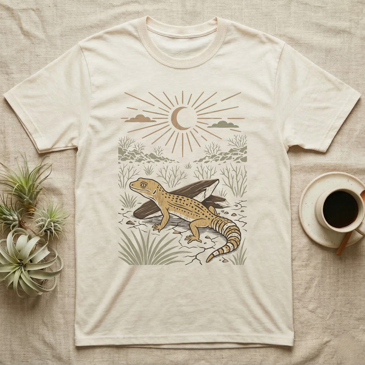 Leopard Gecko Home Range T-Shirt in Natural — Woodcut-style illustration of a leopard gecko standing on cracked earth beside flat stones with thorn scrub behind, no on-shirt text.