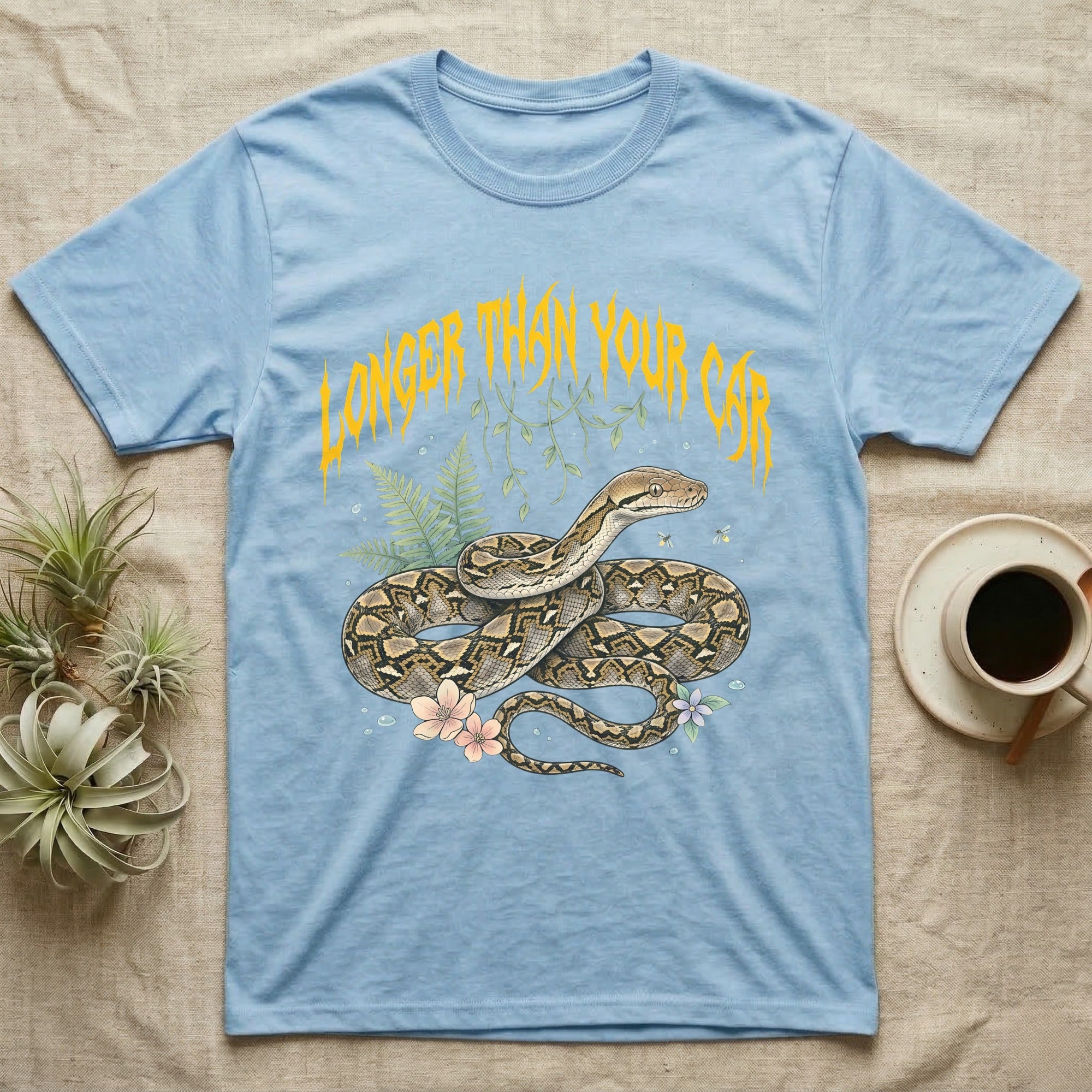 Reticulated Python Feral T-Shirt in Light Blue — Reticulated python in net-patterned coils under jagged molten-gold metal text LONGER THAN YOUR CAR with pastel ferns