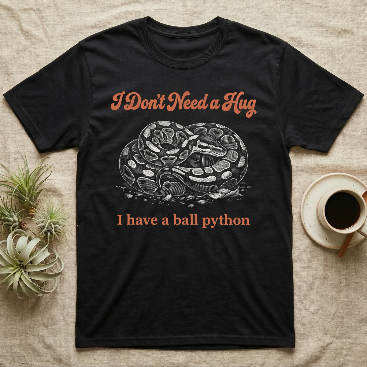 Ball Python Hug T-Shirt in Black — White-line engraving of a coiled ball python under orange script reading I Don't Need a Hug, I have a ball python