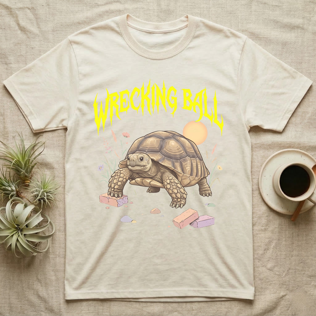 Sulcata Tortoise Feral T-Shirt in Natural — Sulcata tortoise plodding over crumbled bricks under a jagged caution-yellow metal "WRECKING BALL" wordmark.