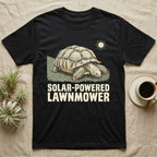 Solar Powered Lawnmower T-Shirt in Black — Retro-illustration of a sulcata tortoise grazing a lawn stripe under a sun motif with a Solar-Powered Lawnmower caption.