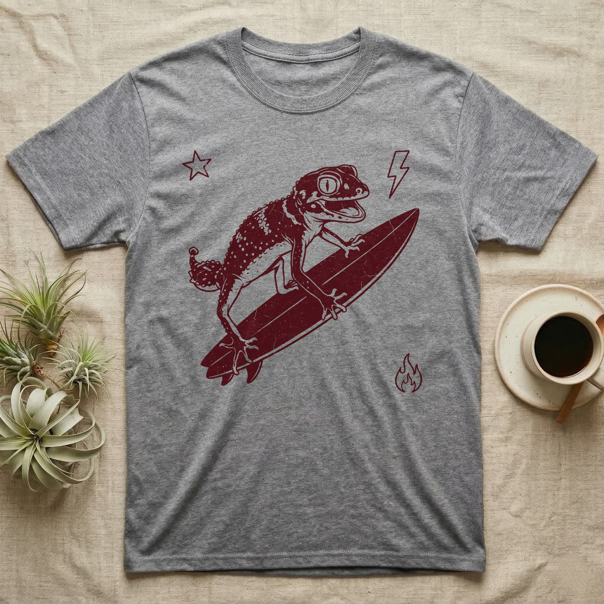 Knob-Tailed Gecko Surfing T-Shirt in Sport Grey — Distressed one-ink illustration of a knob-tailed gecko riding a surfboard, airborne at the peak of an aerial.