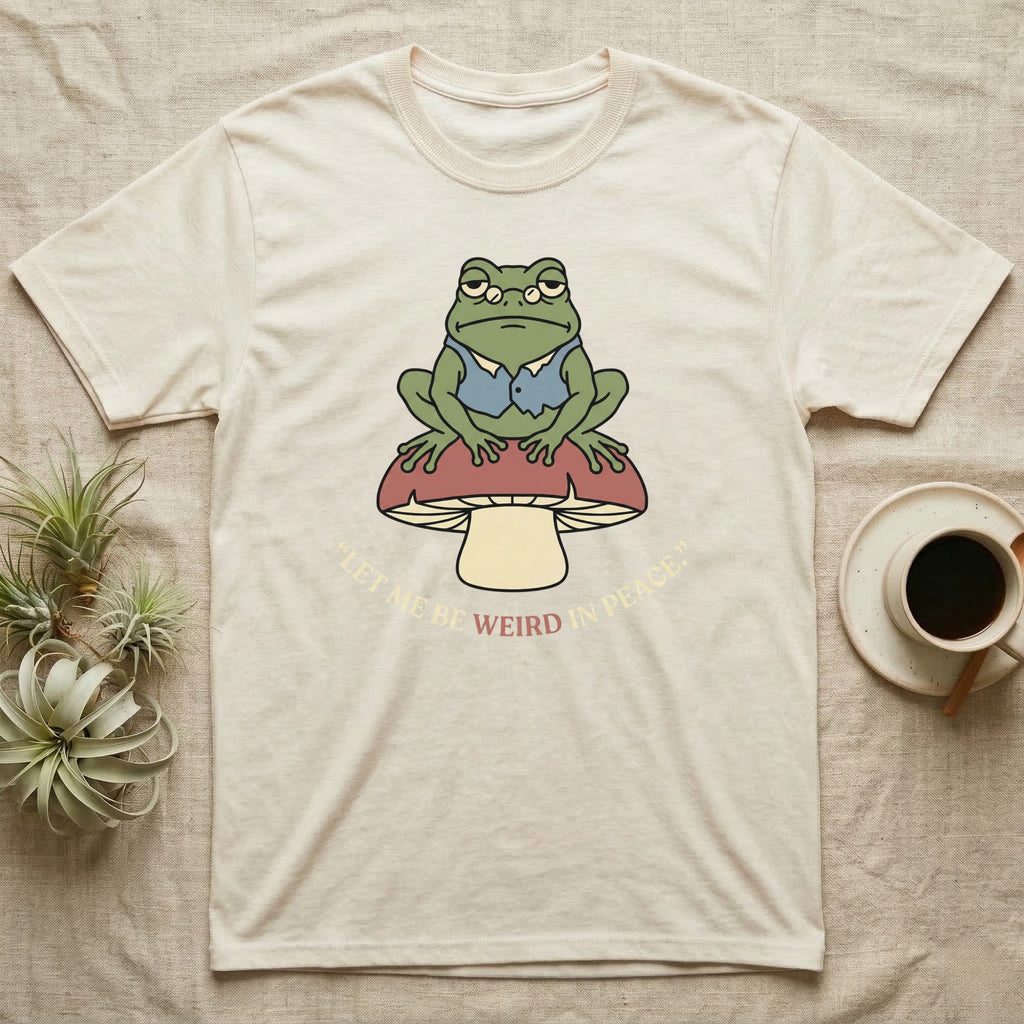 Cream t-shirt with a frog sitting on a mushroom, text "let me be weird in peace".
