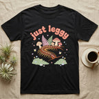 Vietnamese Centipede Baby T-Shirt in Black — Many-legged Vietnamese centipede curving among pastel ferns and toadstools under puffy coral text "just leggy".