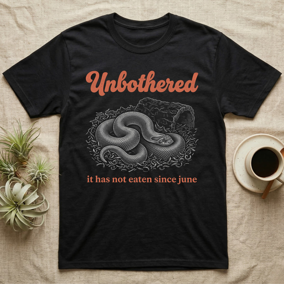 Western Hognose Unbothered T-Shirt in Black — White engraved western hognose snake coiled in loose substrate beside a hide, under the word Unbothered and above it has not eaten since june.