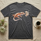 Crested Gecko Blossom T-Shirt in Dark Heather — Watercolor illustration of a rust-brown crested gecko holding a frangipani blossom sprig, on a dark grey t-shirt.