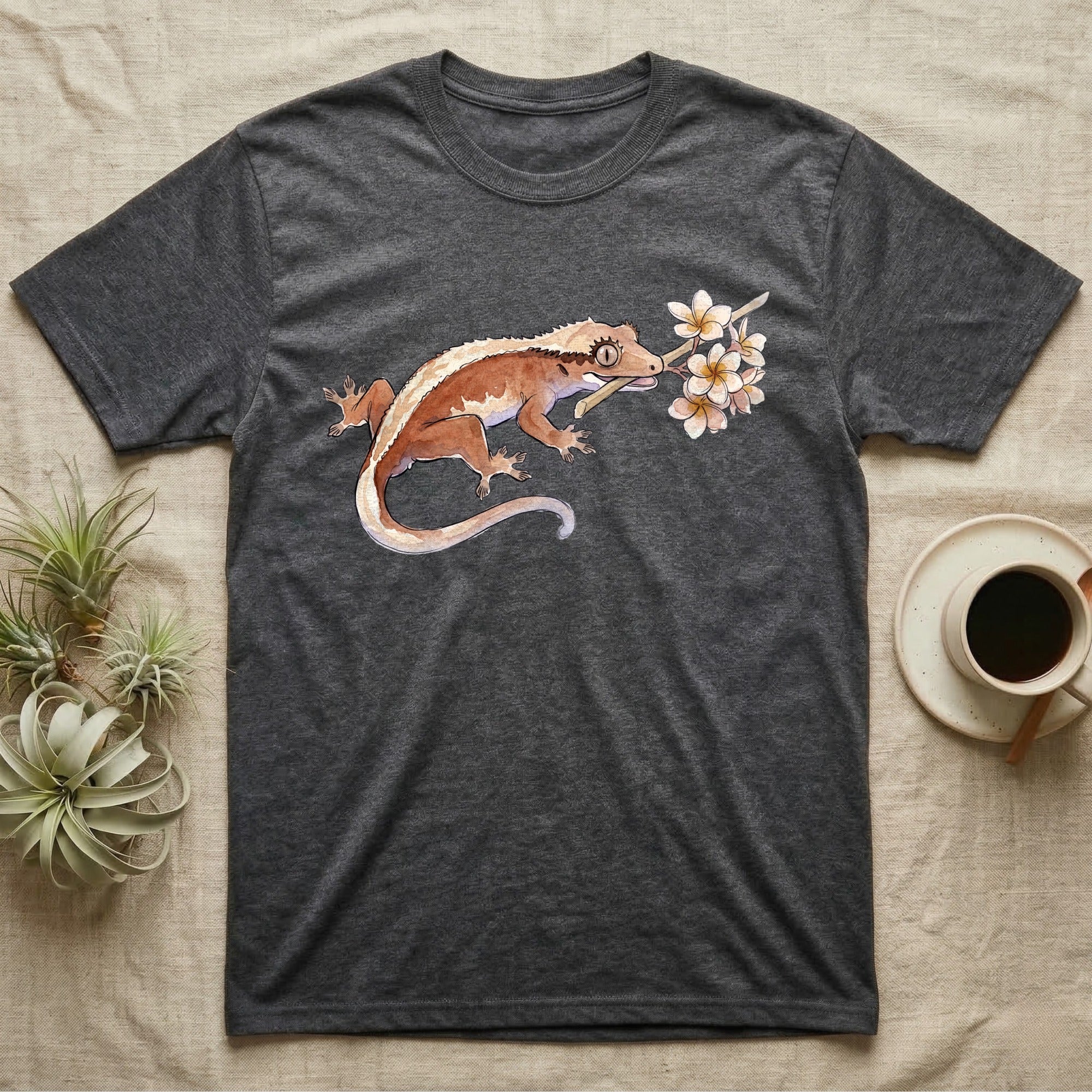 Crested Gecko Blossom T-Shirt in Dark Heather — Watercolor illustration of a rust-brown crested gecko holding a frangipani blossom sprig, on a dark grey t-shirt.