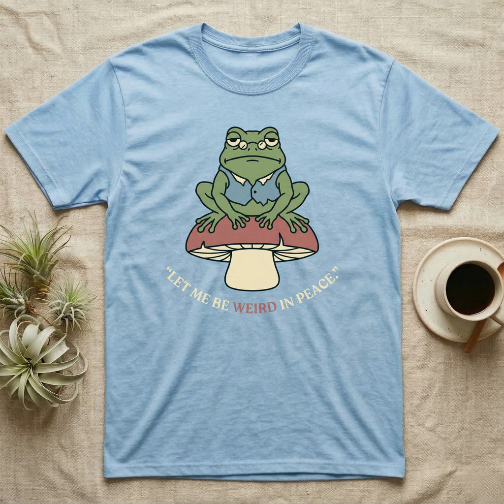 Light blue t-shirt with a frog sitting on a mushroom, text "let me be weird in peace".