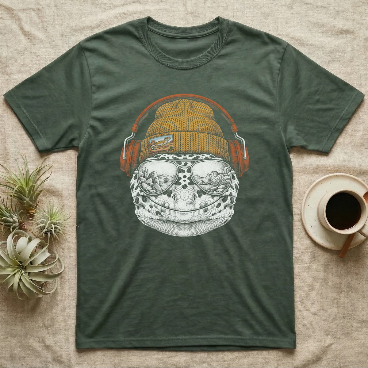 Leopard Gecko Headphones T-Shirt in Military Green — Engraved leopard gecko with spotted skin in a beanie and headphones, aviators reflecting a desert canyon.