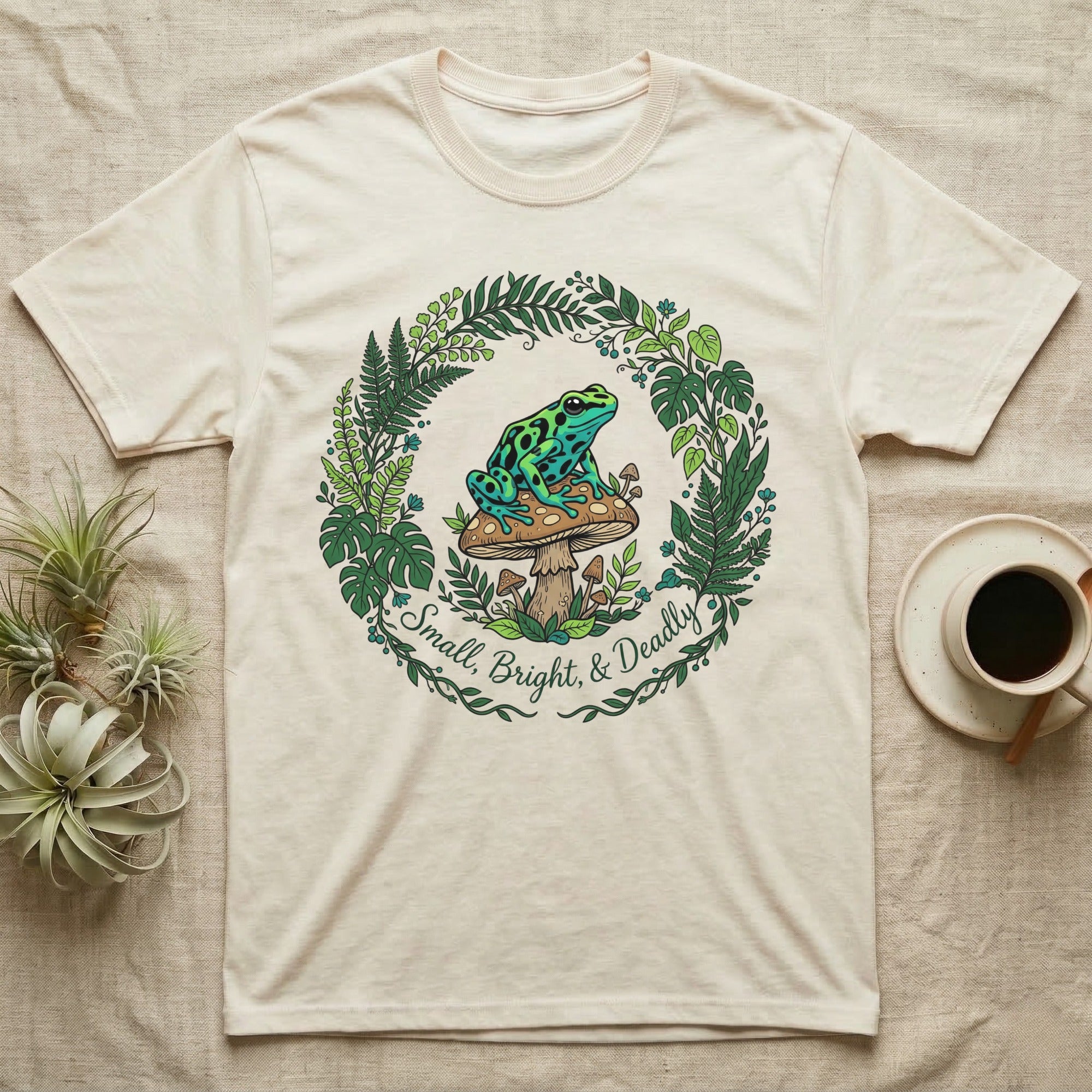 Cream t-shirt with green frog on mushroom graphic and text "Small, Bright, & Deadly".