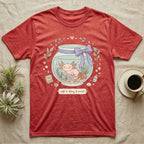 Red t-shirt with axolotl in a jar, surrounded by plants, food, and water conditioner.