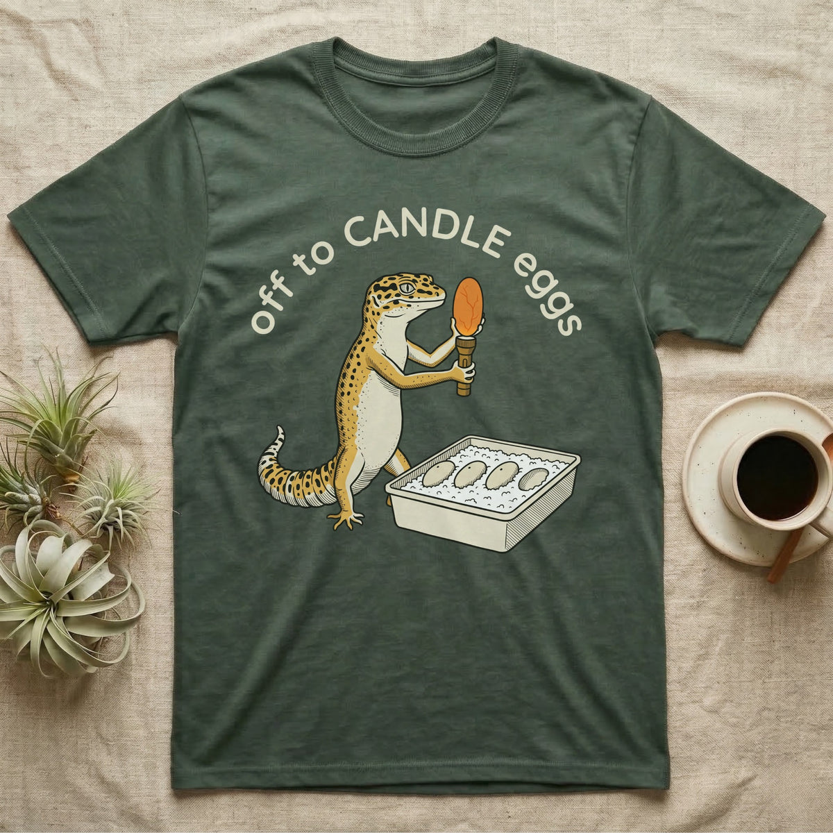 Leopard Gecko Candling T-Shirt in Military Green — Leopard gecko holding a torch under a glowing orange egg beside a tub of eggs, under the words off to CANDLE eggs