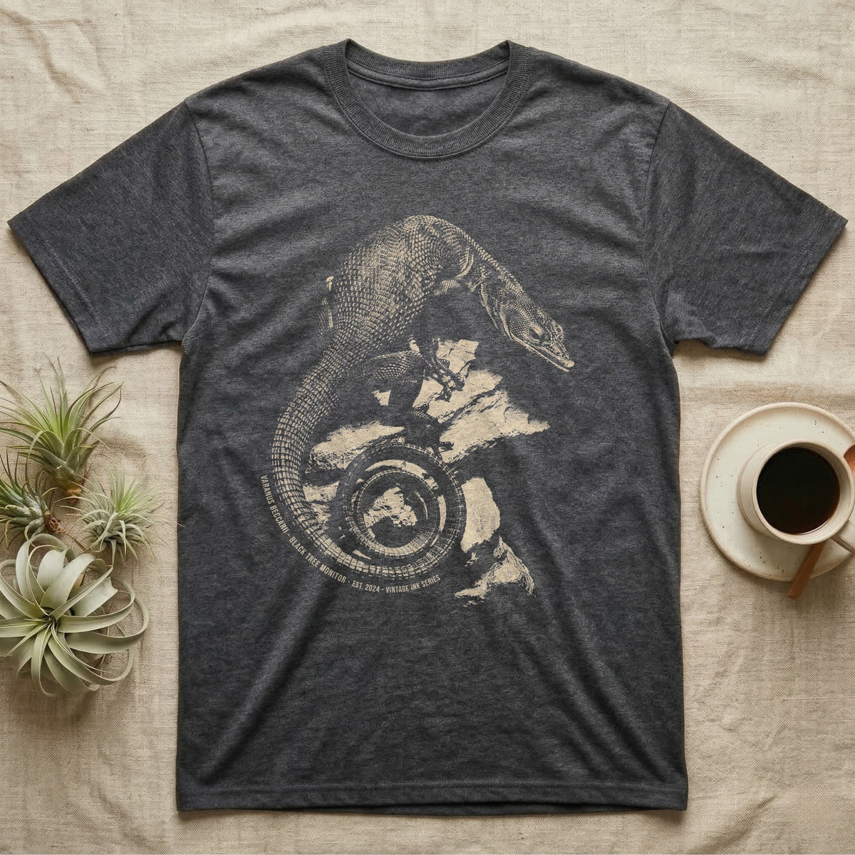 Vintage engraved illustration of a black tree monitor climbing rock with its tail coiled into a badge, arc text reading Varanus Beccarii, Black Tree Monitor, Est. 2024, Vintage Ink Series. — shown on a Dark Heather tee.