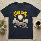 Moroccan Uromastyx Feral T-Shirt in Navy — Moroccan uromastyx basking under a big sun with a jagged solar-gold metal "SUN GOD" wordmark and pastel desert scene.