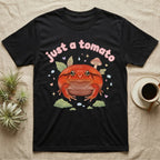 Tomato Frog Softie T-Shirt in Black — Round red-orange tomato frog facing forward under a puffy pastel "just a tomato" bubble wordmark with tiny hearts.