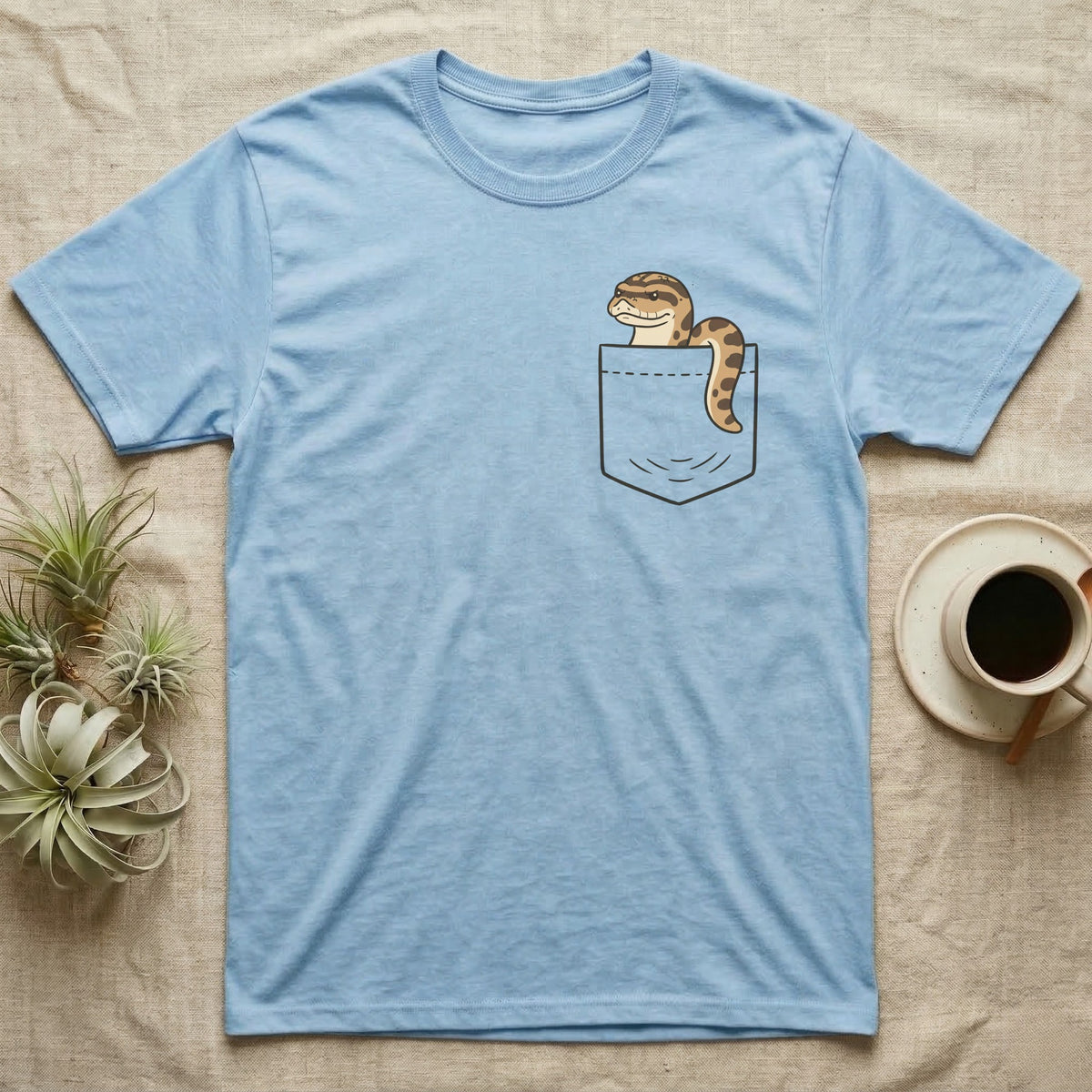 Hognose Pocket T-Shirt in Light Blue — Cartoon western hognose with an upturned snout peeking out of a chest pocket, its body looped over the edge