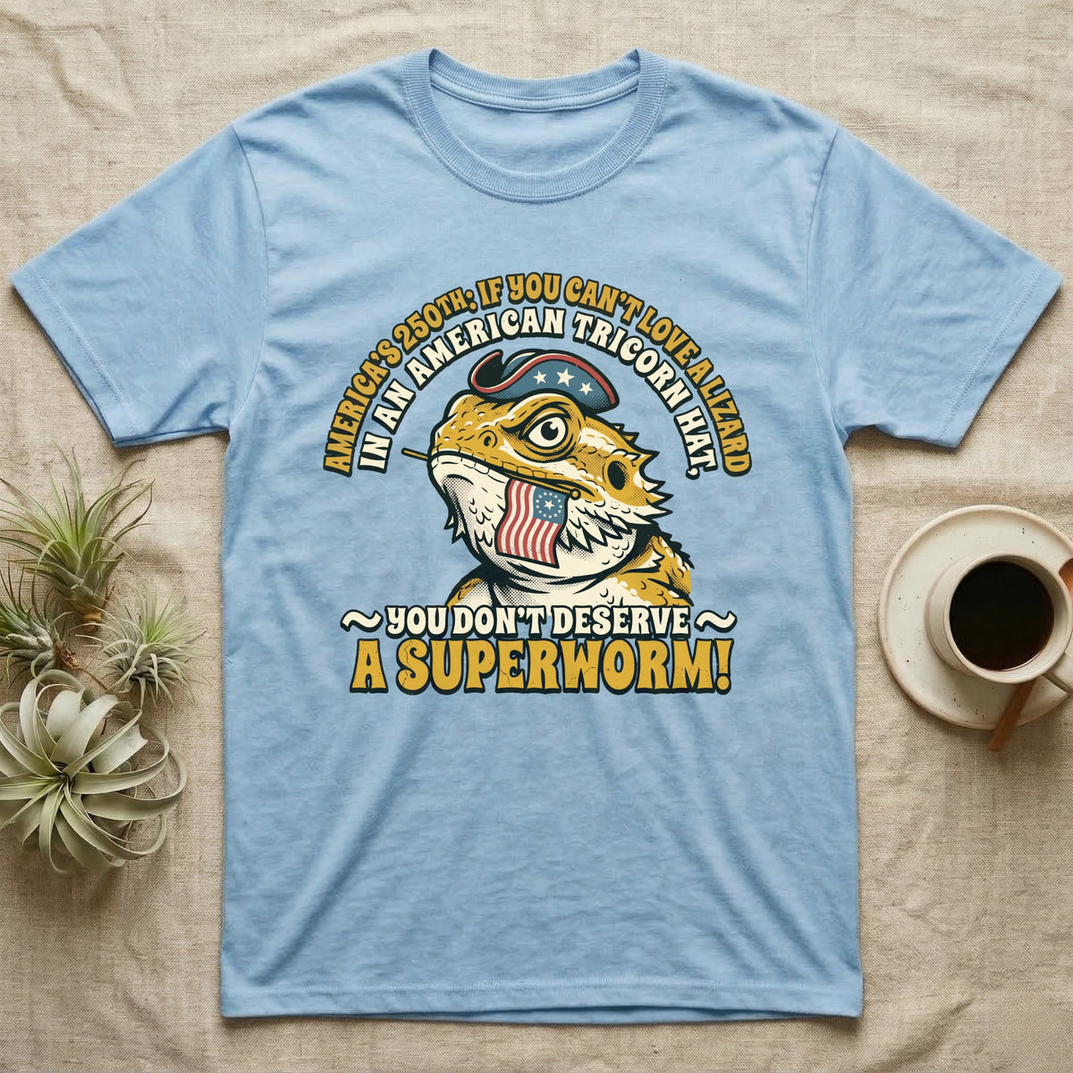 Bearded Dragon Tricorn Tee in Light Blue — Bold woodcut tee of a bearded dragon in a colonial tricorn hat, gold and cream text reading You Don't Deserve A Superworm, on black.