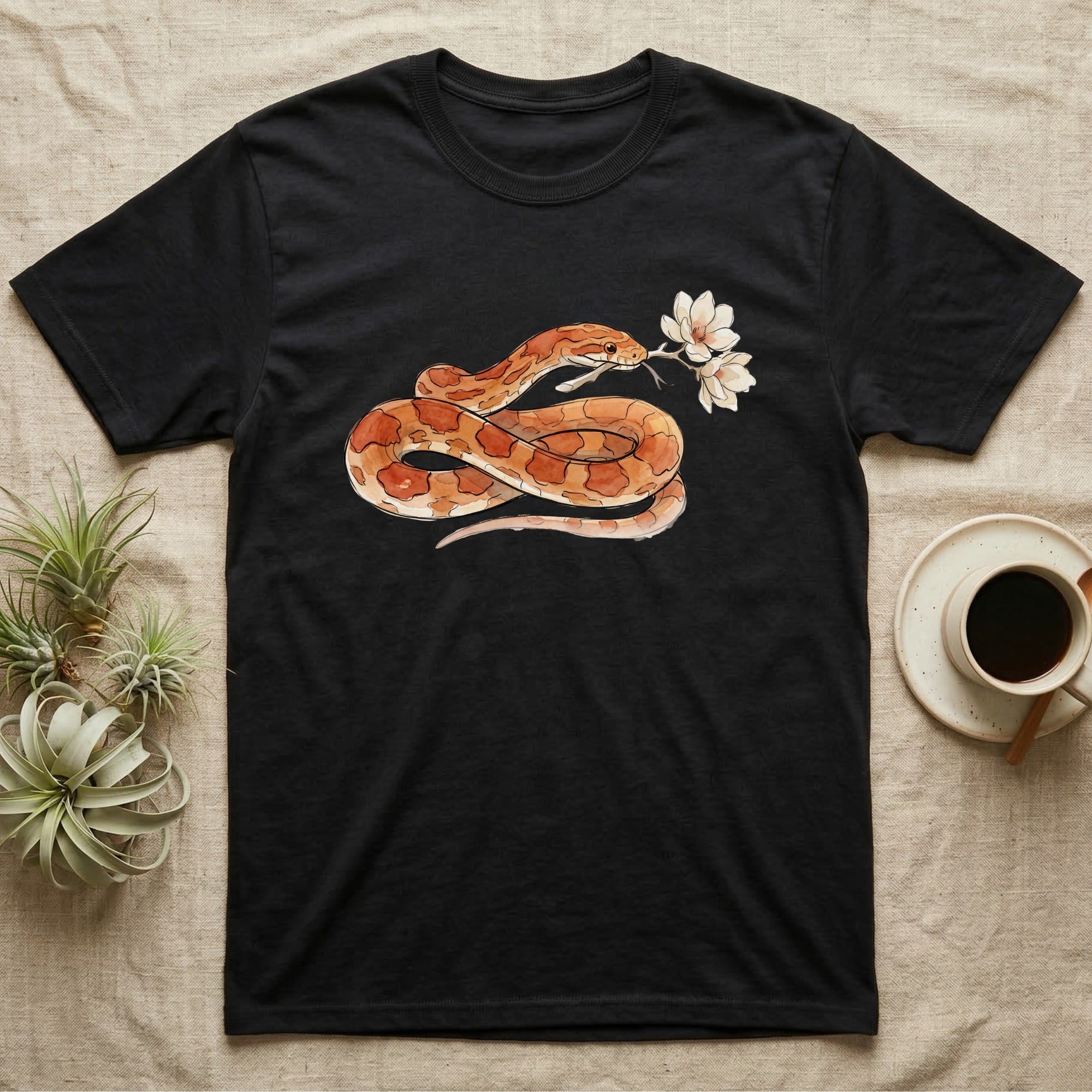 Corn Snake Blossom T-Shirt in Black — Watercolor illustration of an orange-and-cream corn snake holding a magnolia blossom sprig, on a dark grey t-shirt.