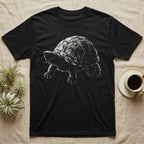 Musk Turtle Stinkpot T-Shirt in Black — Rim-lit negative-space illustration of a small musk turtle in badge-scale portrait against a dark ground.