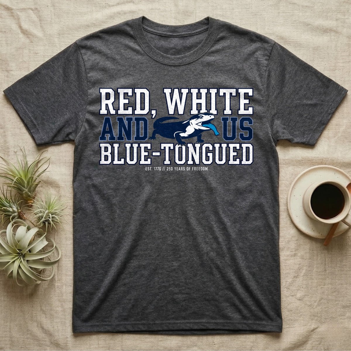 Blue-Tongued Skink 1776 T-Shirt in Dark Heather — Navy and white blue-tongued skink with tongue out between collegiate text reading Red, White and US Blue-Tongued.