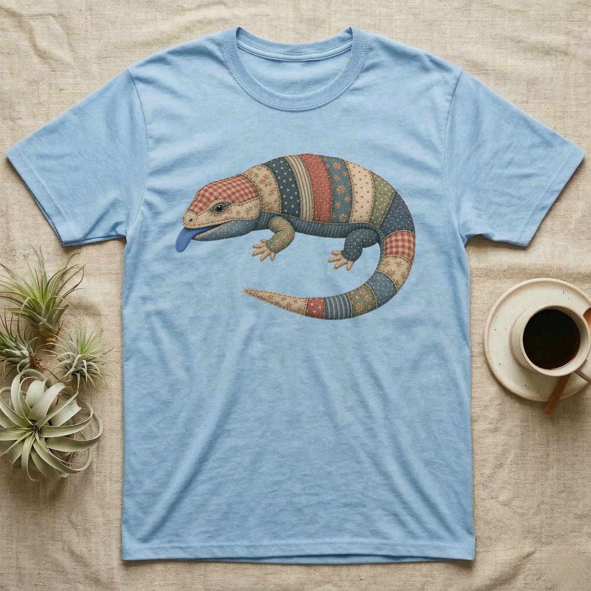 Light blue t-shirt with a colorful, patchwork lizard graphic and blue tongue.