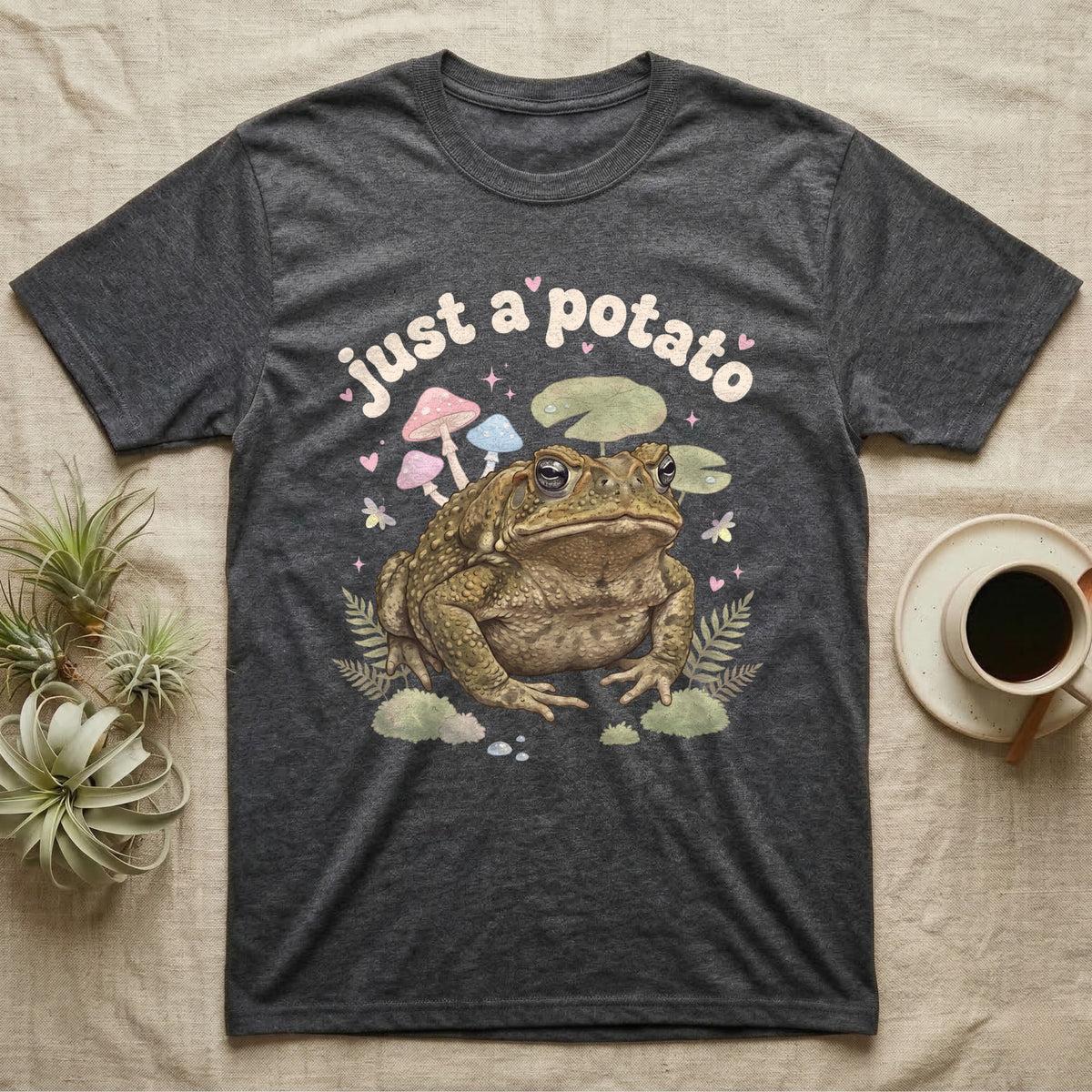 Cane Toad Baby T-Shirt in Dark Heather — Warty cane toad among pastel toadstools and lily pads under puffy cream bubble text "just a potato".