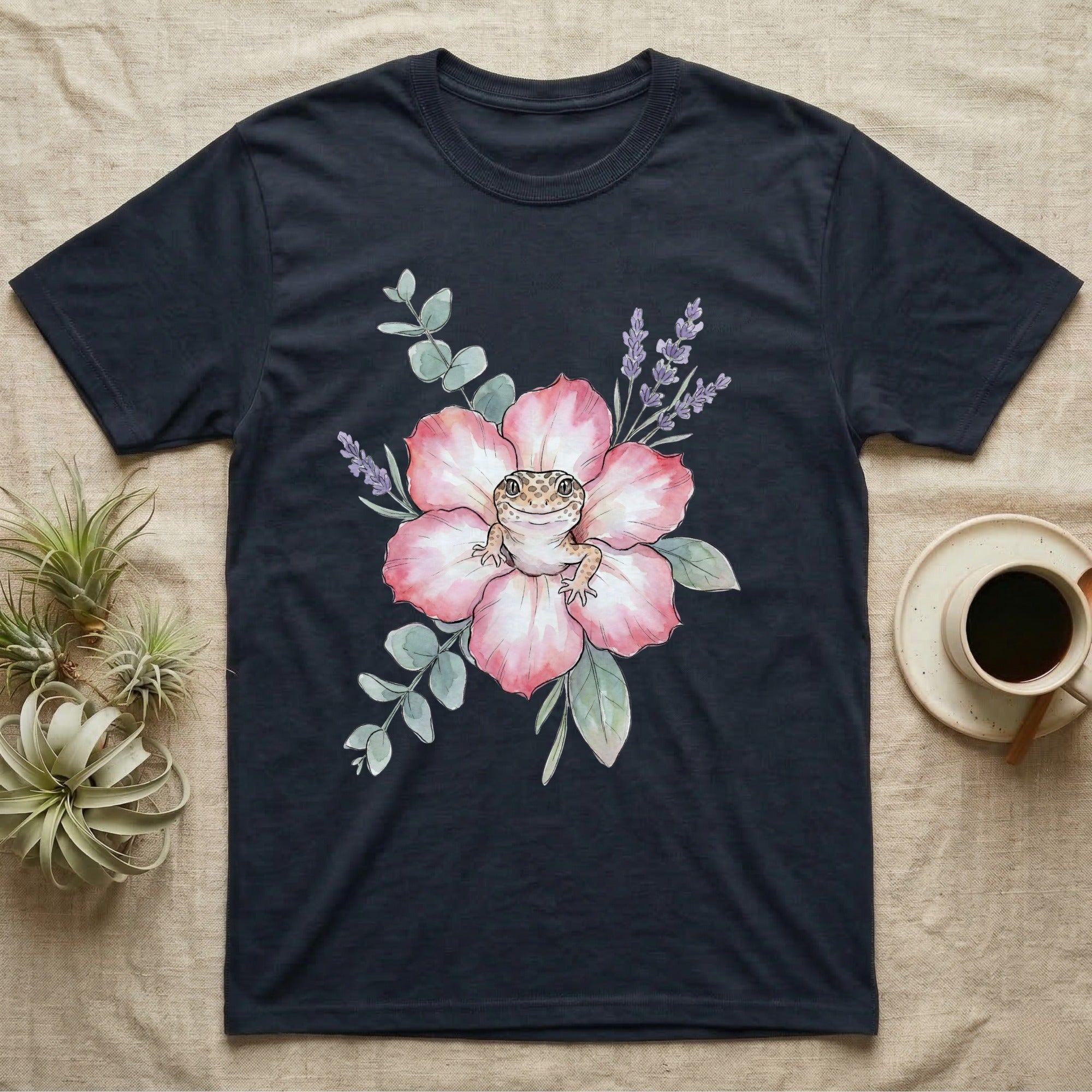 Dark t-shirt with a watercolor illustration of a gecko on a pink flower with lavender sprigs.